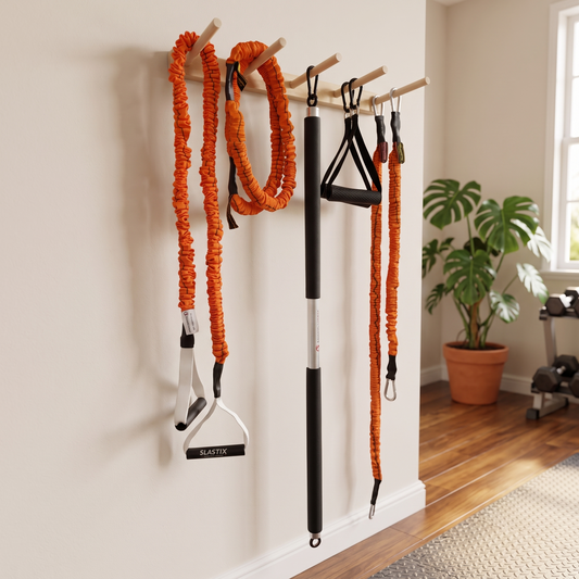 A set of home workout resistance bands and handles hanging from a wooden peg rack mounted on a beige wall in a home gym. Visible brands include BLASTX on the handles.
