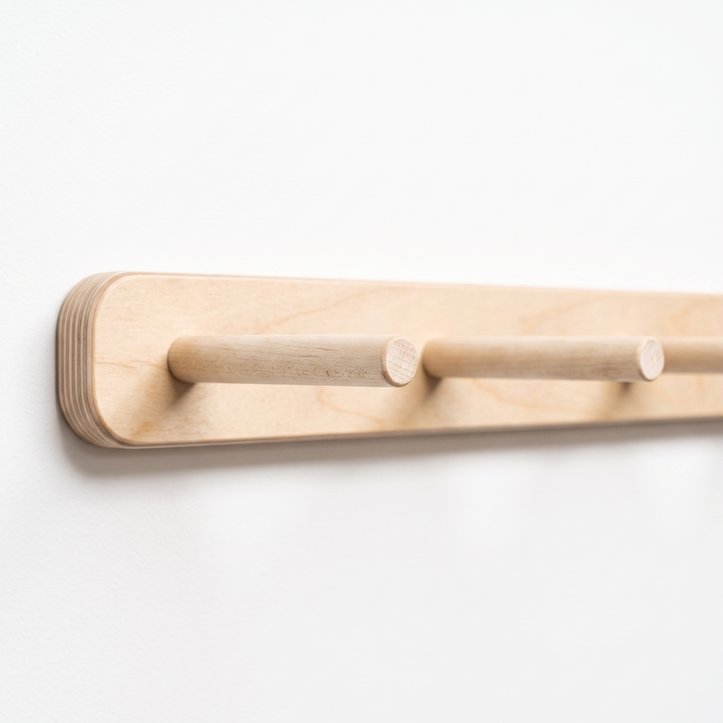 A close-up of a light natural wood wall-mounted coat rack with two round peg hooks on a plain white background.