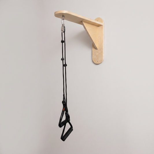 A wall-mounted wooden support bracket holding a black resistance tube exercise strap with handles, shown against a plain light gray wall.