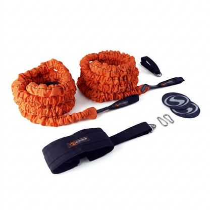 An orange elastic resistance band set with black handles, a black wrist strap, two black circular weight plates, and metal clips, displayed on a clean white background.