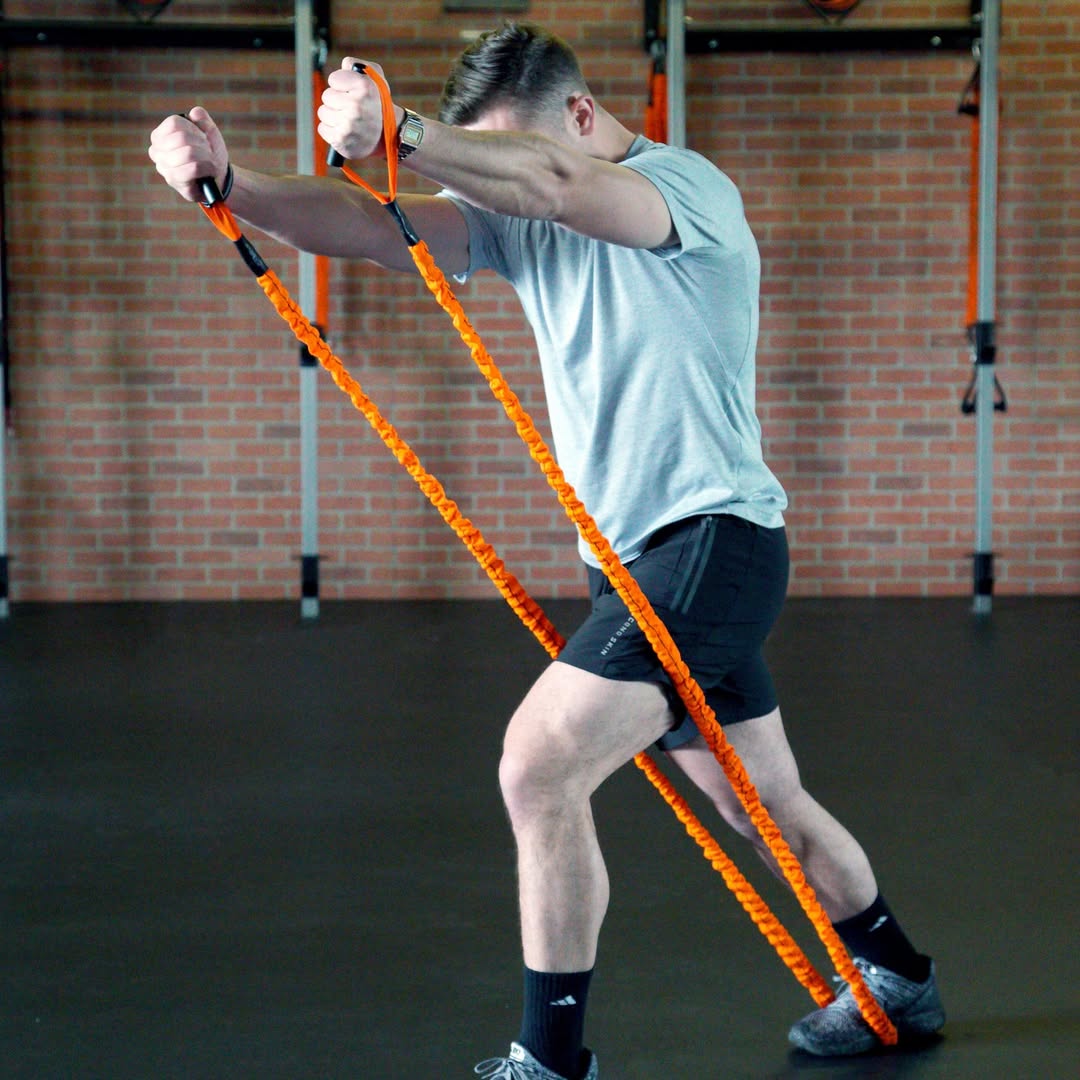 Person using orange resistance bands in a gym setting with brick walls.