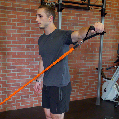 Man using an orange resistance band in a gym setting with a brick wall background